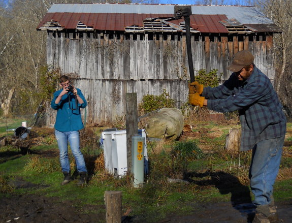 using a Chopper 1 axe to split wood with someone taking a picture in the background