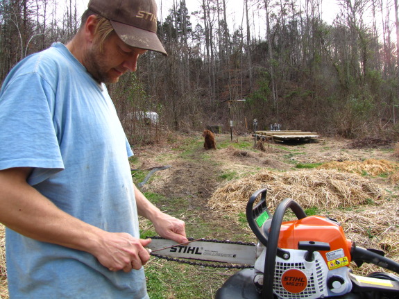 man sharpen chainsaw chain with file complete with dog in background